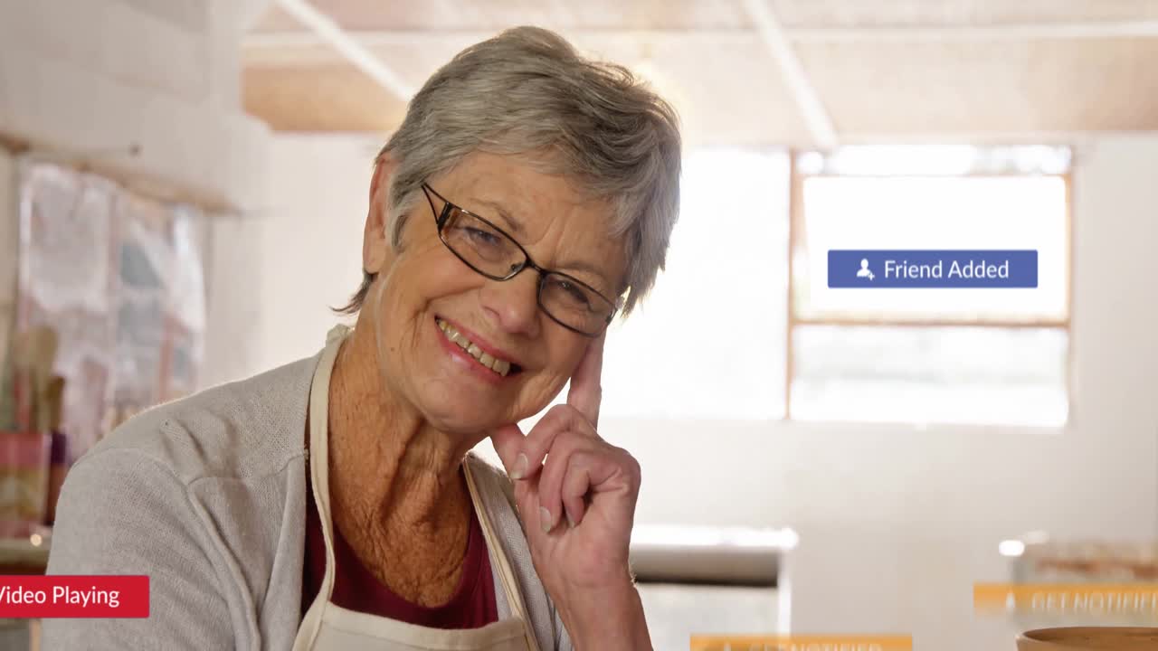Senior woman wearing apron smiling in pottery shop with floating social media alert icons