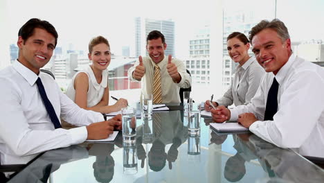 Laughing-businessman-giving-thumbs-up-with-colleagues-around