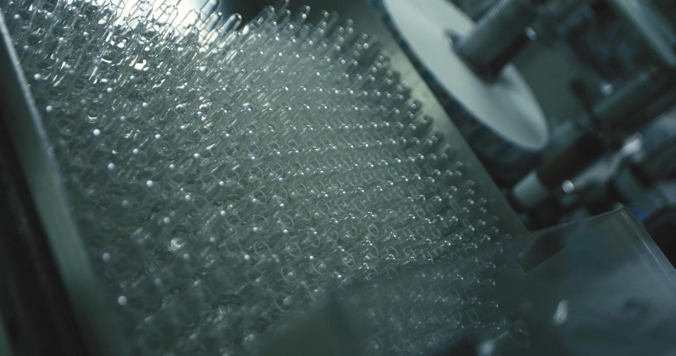 Gloved hand carefully inspecting rows of empty glass vials in a sterile pharmaceutical manufacturing facility