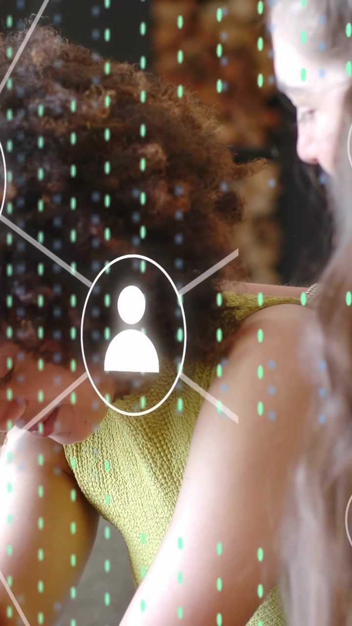 Vertical video: Two women leaning in as user icon appearing forming net overlay for collaboration