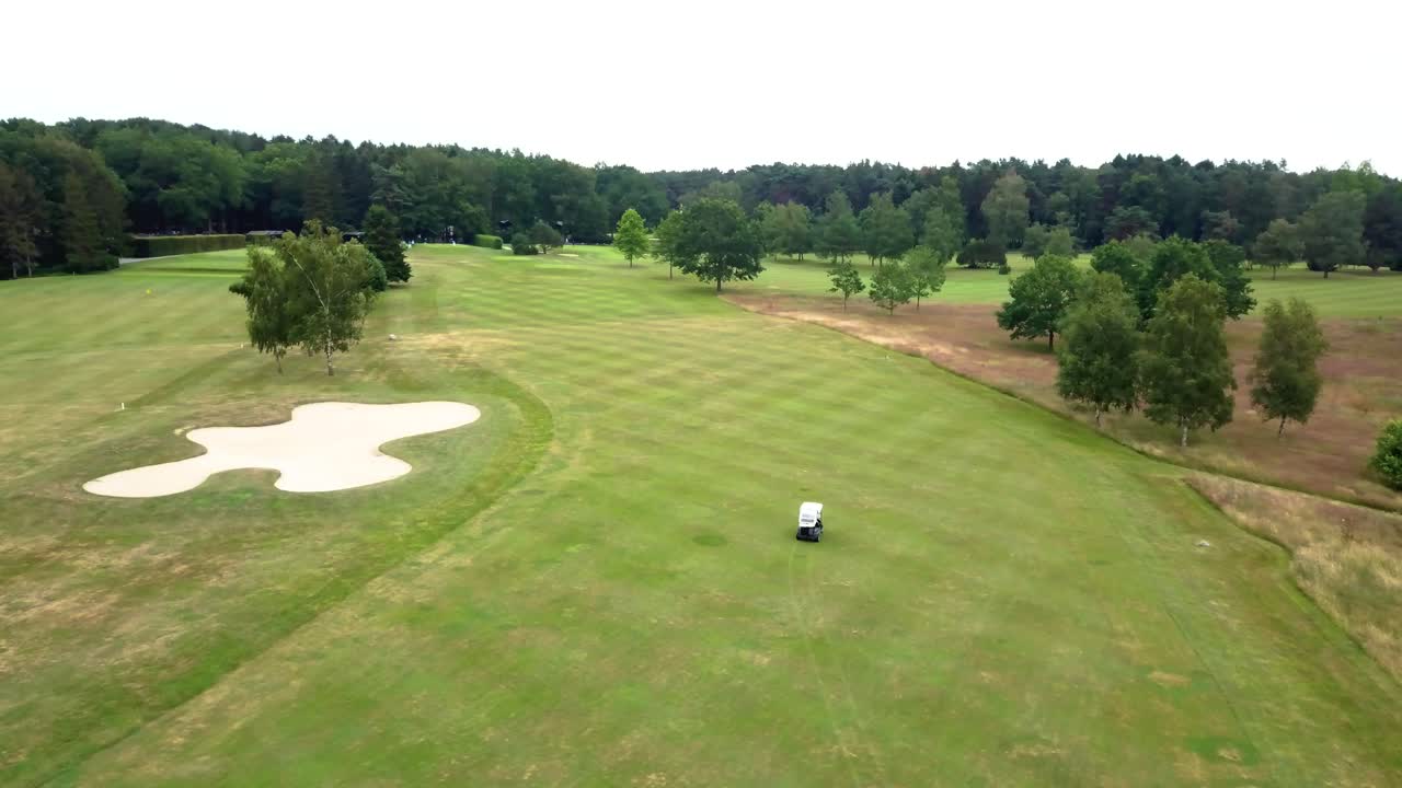 Drone video of a golfer driving golf cart car on a golf course between forest trees