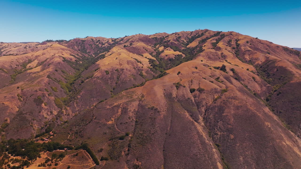 Rising above mountains, bare brown rocks with no vegetation, rock with moss. Rocky coastline of California at backdrop of blue clear sky. Aerial view.