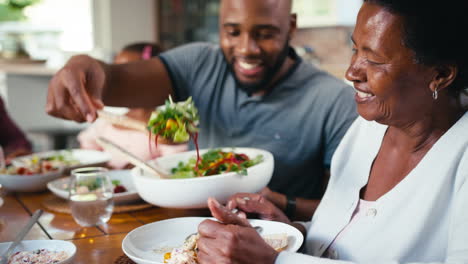 close up of multi-generation family sitting around table serving food for meal at home together