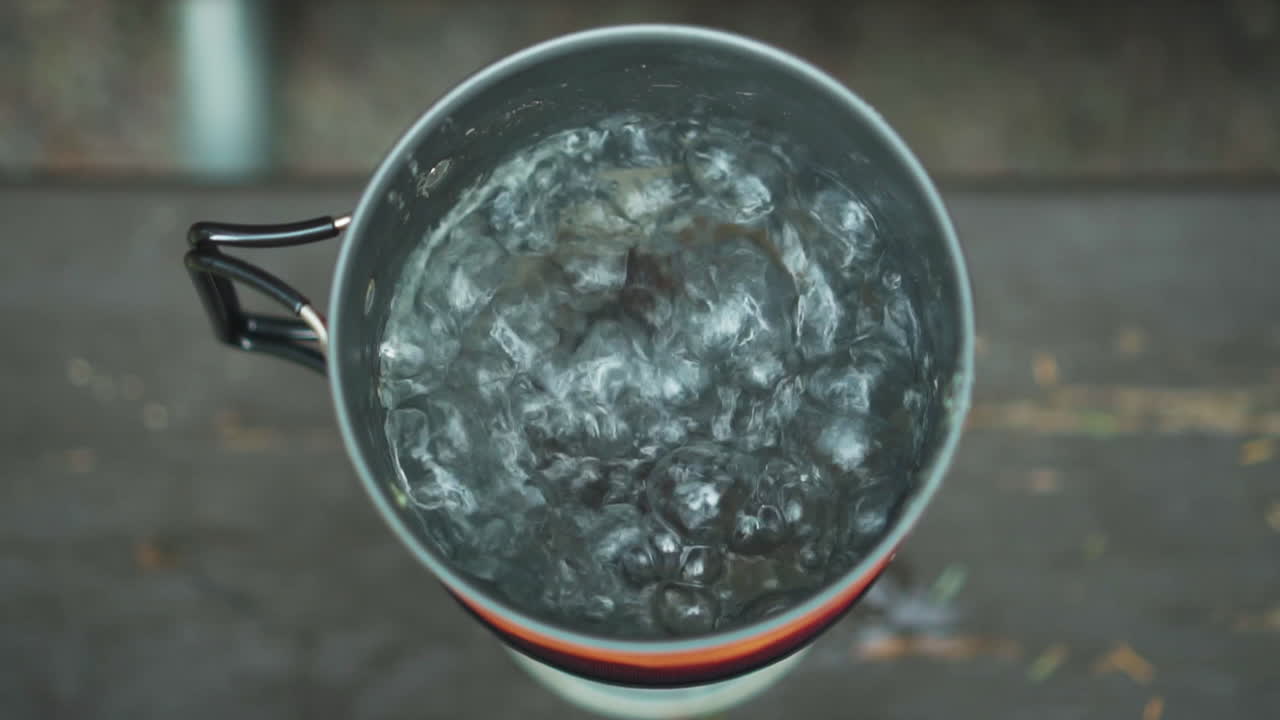 Close up overview of travel gas burner and small pot with boiling and steaming hot water at Glacier NP Campground and Creek camp site in USA