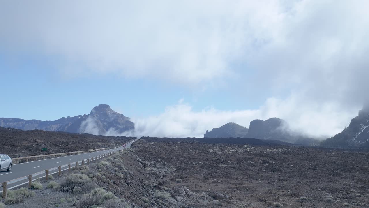 Auto che guidano su una strada panoramica attraverso montagne vulcaniche e nuvole.
