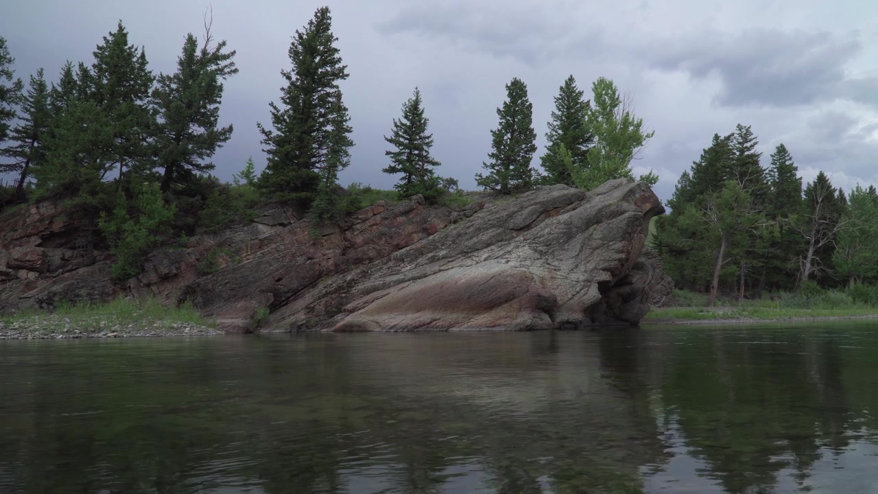Inquadratura ampia di una grande roccia, circondata da alberi, skyline e un fiume