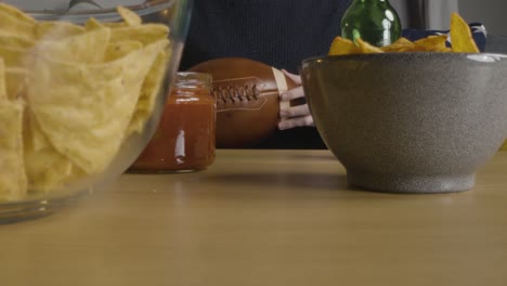 person at home watching american football game on tv with drinks snacks and ball 5