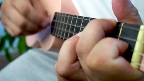 hombre de mediana edad 30 y con cuentas está jugando y silbando con su ukulele rosado al lado de una gran ventana y cerca de una planta verde