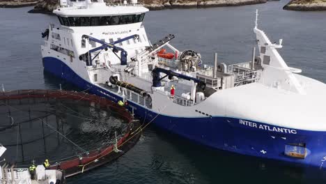 ascending drone shot of workers maintaining a fish farming cage on a boat