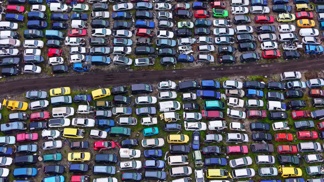 Stor samling af parkerede biler på en bilkirkegård om dagen nær en by