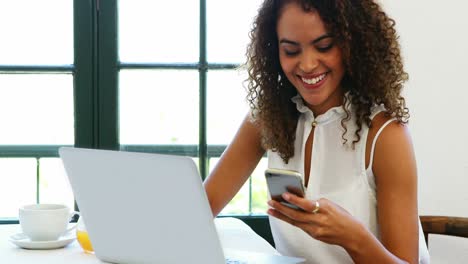 Woman-using-mobile-phone-while-working-on-laptop-4k