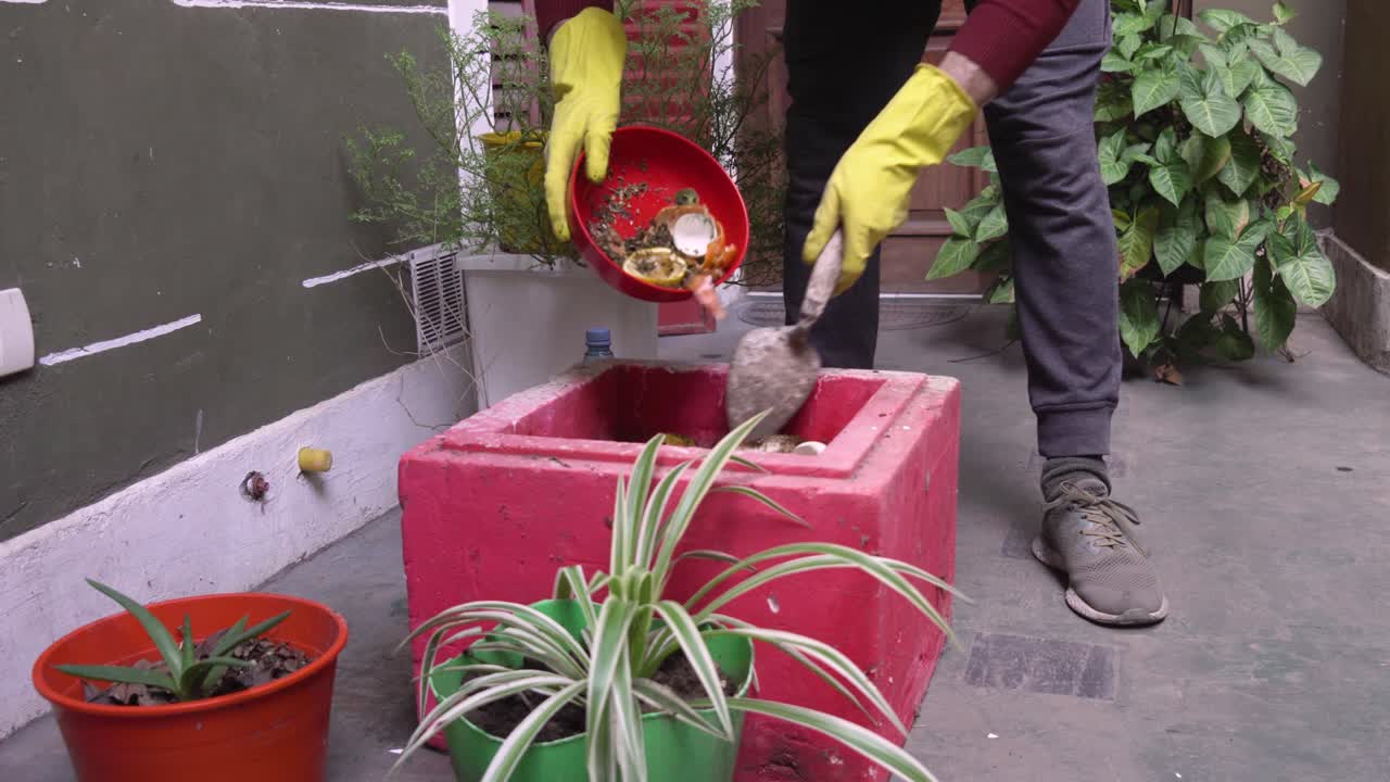 un tipo en un jardín de la ciudad compacta agrega material orgánico a un contenedor de compost