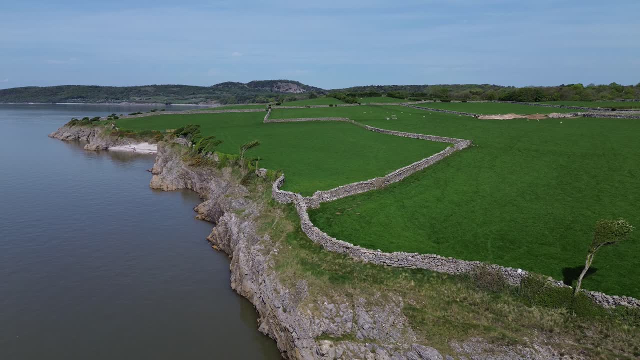 Lake district coastal farmland aerial view descends to stone wall boundary overlooking Morecambe bay