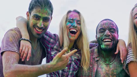 close up of the young mixed races cheerful friends in colorful paints during holi festival hugging and laughing to the camera