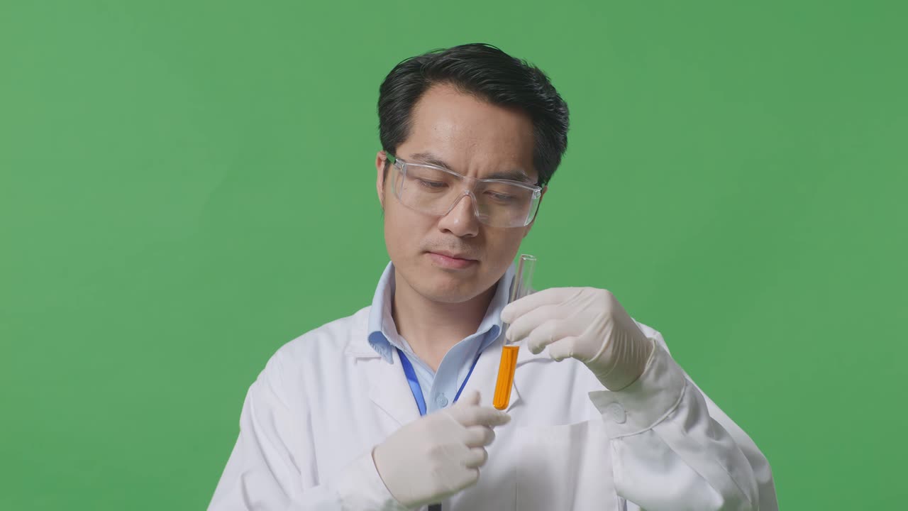 Close Up Of Asian Man Scientist With Orange Liquid In The Test Tube Thinking And Looking Around Then Raising His Index Finger On The Green Screen Background In The Laboratory