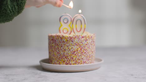 bolo de aniversário de foto de estúdio coberto com enfeites e vela comemorando o octogésimo aniversário sendo aceso