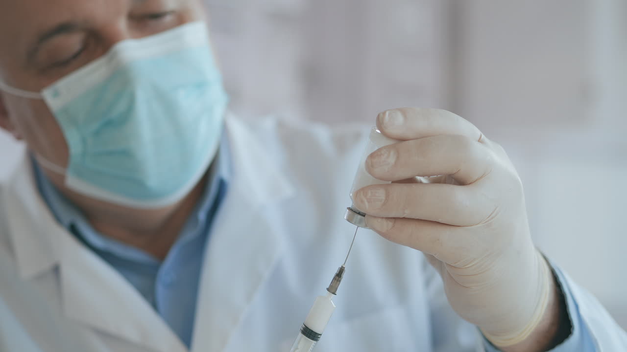 doctor hand holds a syringe and a blue vaccine bottle at the hospital. Health and medical concepts. doctor draws vaccine to syringe vial covid-19 coronavirus ampoule injection. High quality 4k footage
