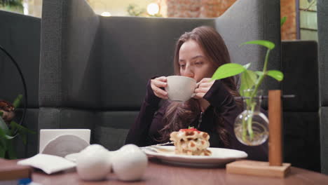lady holds white cup close to lips while sipping latte in stylish booth adorned with decorative vase, waffles on plate, and serene ambiance, conveying peaceful indoor coffee moment with elegance