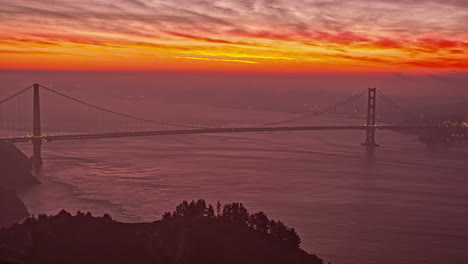 Toma-Estática-Del-Movimiento-De-Las-Nubes-Sobre-El-Cielo-Rojo-Y-Amarillo-Durante-El-Amanecer-En-El-Lapso-De-Tiempo-Sobre-El-Conocido-Puente-Golden-Gate