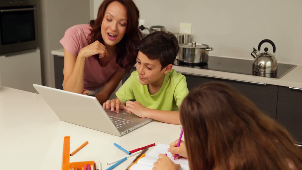 madre usando computadora portátil con el hijo mientras la hija está dibujando
