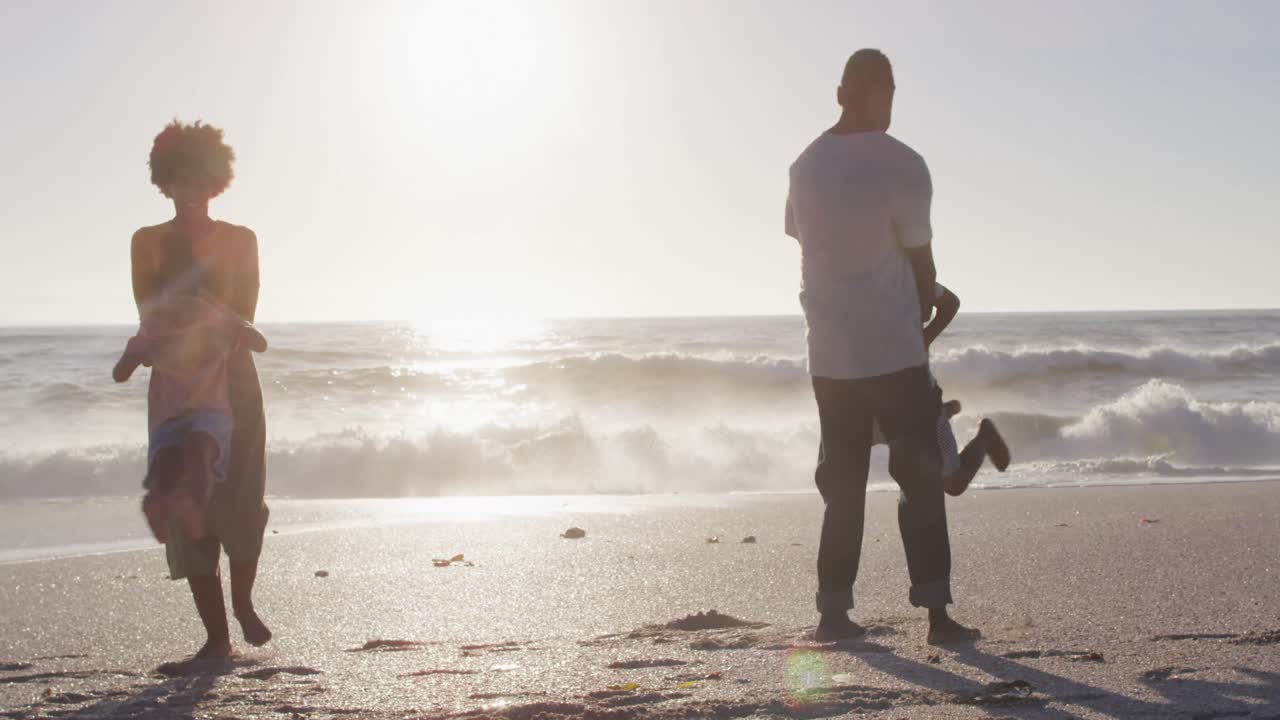 웃는 아프리카계 미국인 가족이 손을 잡고  ⁇ 은 해변에서 놀고 있습니다.