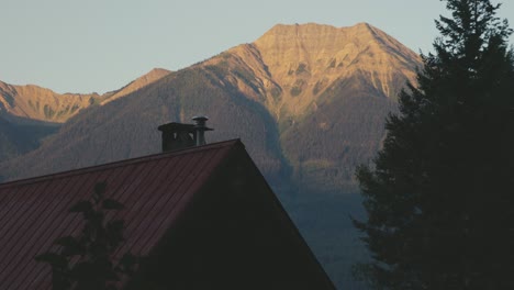 a charming house located in the woods of canada near golden and banff national park, with a huge mountain in the background, during sunrise hours