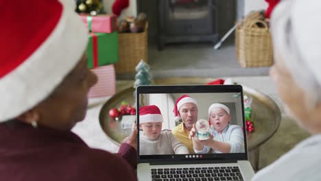 Diverse-senior-female-friends-using-laptop-for-christmas-video-call-with-smiling-family-on-screen