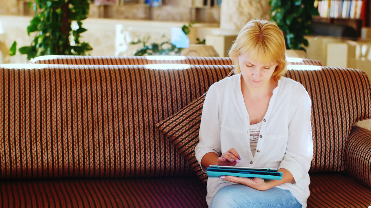 Woman In A Summer Shirt Uses A Tablet In The Hotel Lobby