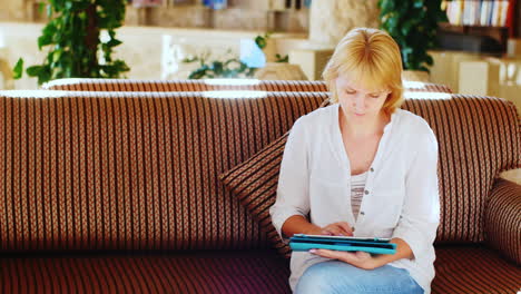 Woman-In-A-Summer-Shirt-Uses-A-Tablet-In-The-Hotel-Lobby