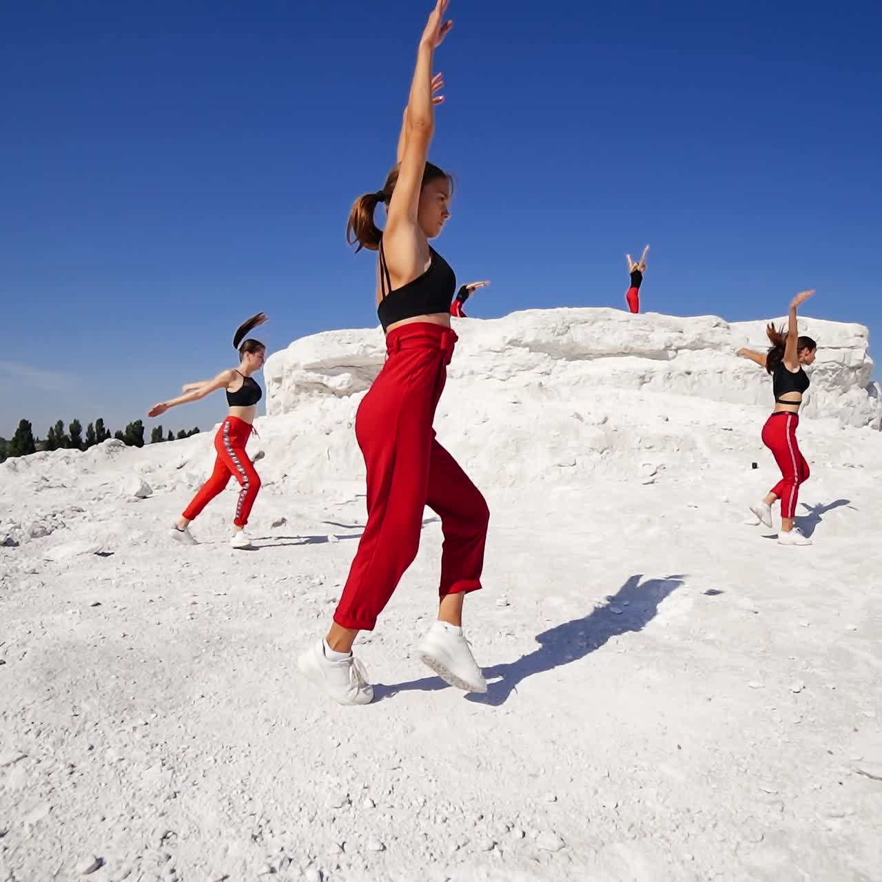 Girls wearing similar clothes dancing on a white rocky land. Teenage dance studio performing outdoors on sunny day