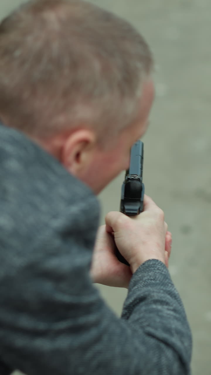 una vista de cerca desde atrás de un hombre en una chaqueta gris apuntando una pistola a un objetivo invisible por un camino desierto