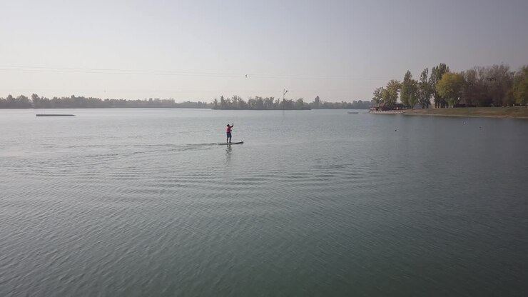 Drone shot of a person paddle boarding on a lake on a sunny day