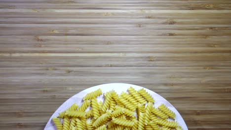 pasta de fusilli cruda que gira sobre una tabla de cortar en blanco, en bucle