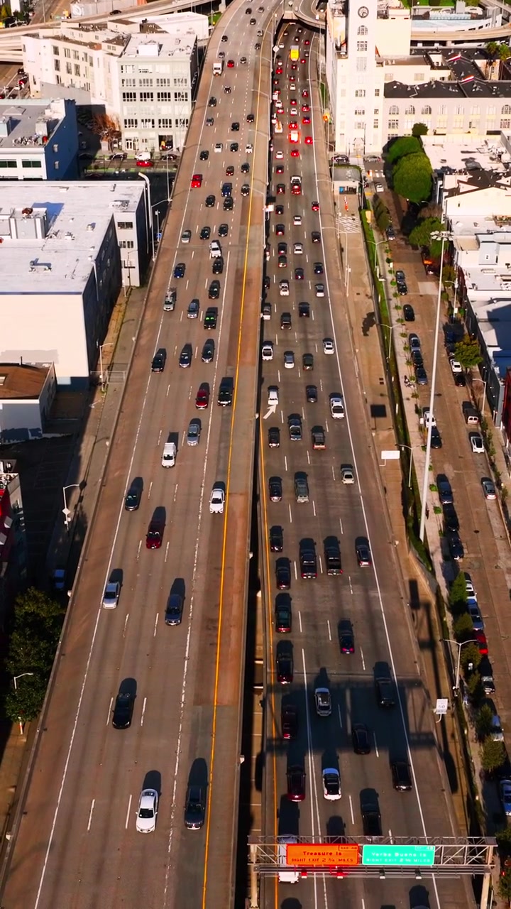 Vista aérea del tráfico en una autopista de varios carriles, San Francisco, California. Ángulo cenital que captura una torre del reloj, una calle de la ciudad y vehículos estacionados. Video vertical