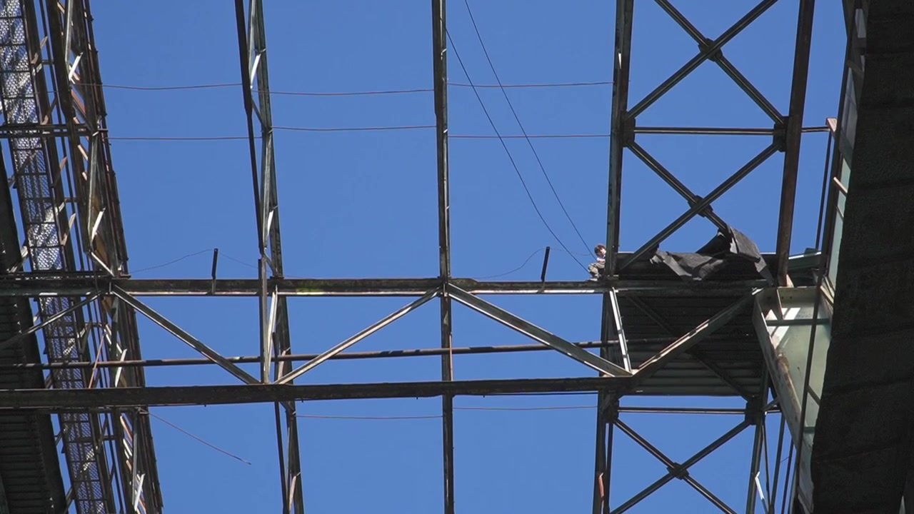 A worker is positioned on a steel framework, ensuring stability against a bright blue sky. This shot captures the essence of industrial labor and construction safety. Ideal for construction industry v