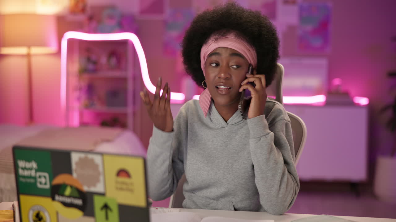 한 젊은 여성 이 집 에서 책상 에서 일 하면서 전화 로 이야기 하고 있다