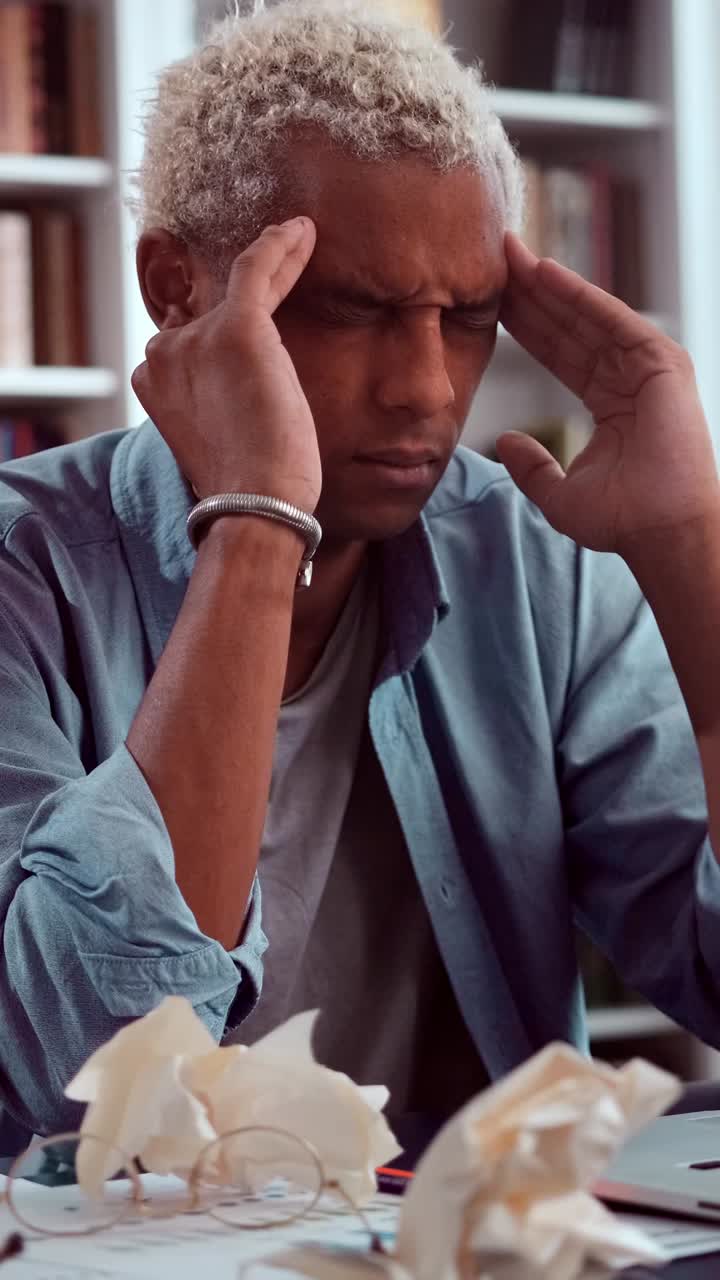 Stressed young creative professional sitting at a cluttered desk holding his