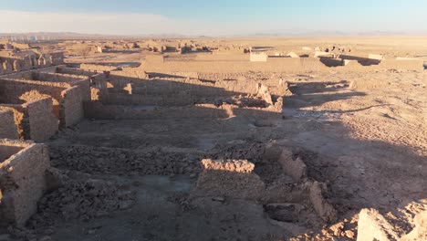 close-up drone shot of the ruined adobe facades of a former saltpeter works, close flight moving forward into the sunset in the desert