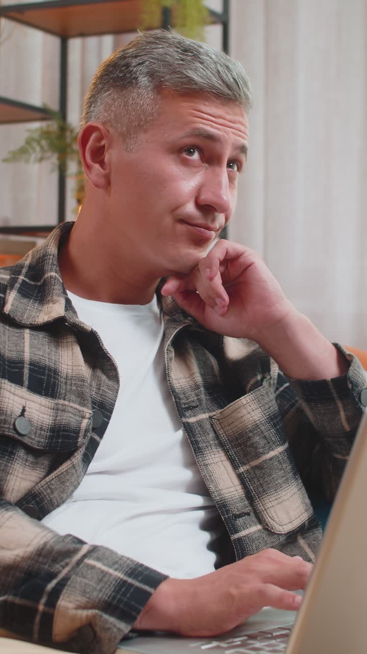 Man working on laptop computer with pensive expression pondering a solution answer at home room