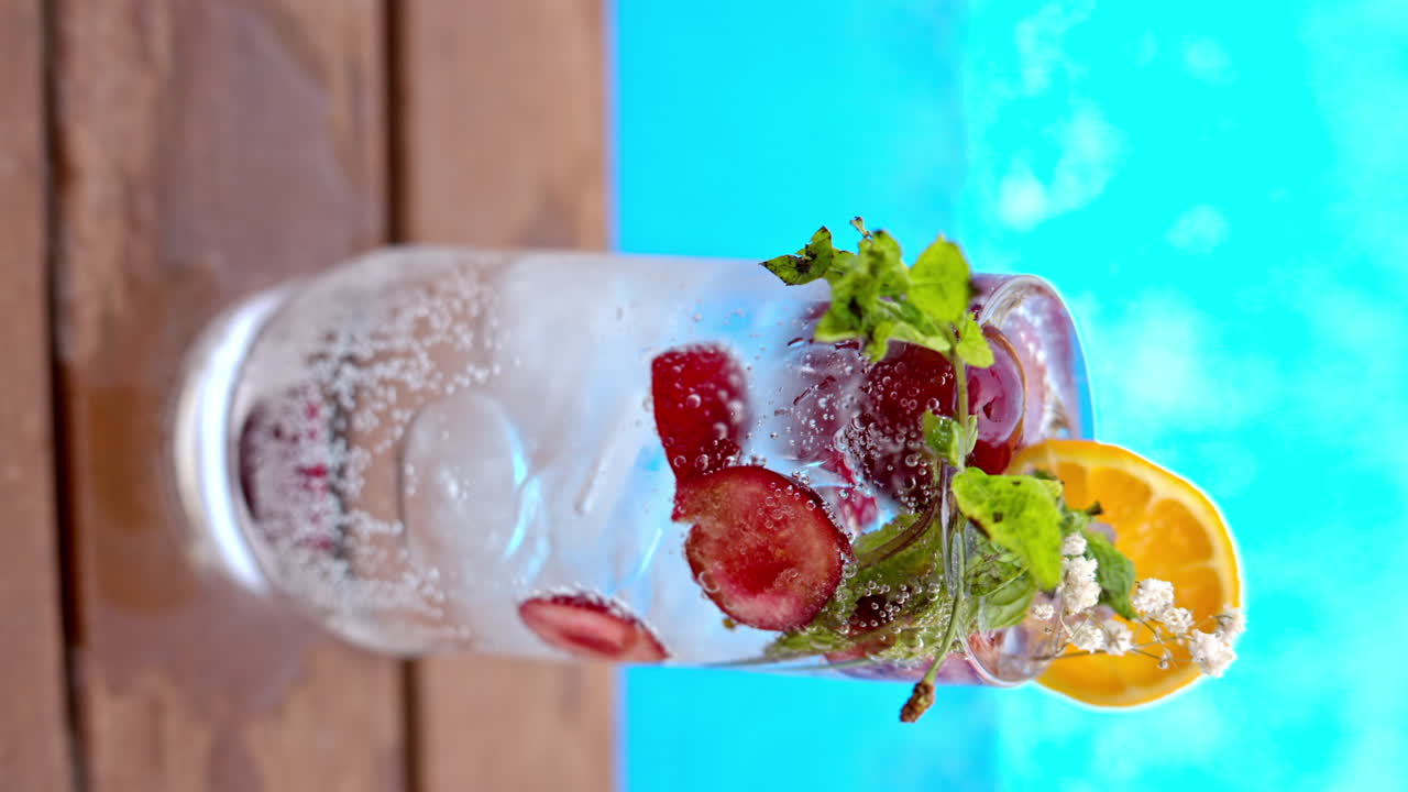 Mojito cocktail glass with ice and cherry and mint, soda and gin near a blue pool close up