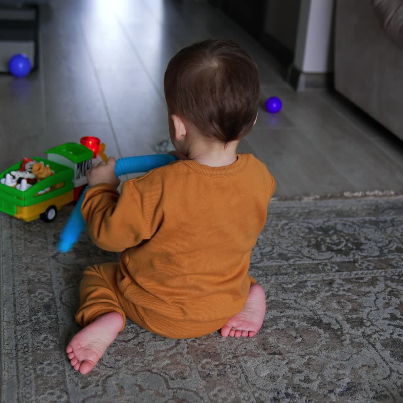 Barefoot lovely kid sitting on the floor his back to the camera. Lovely child plays with a part from toy happily. Toy around child