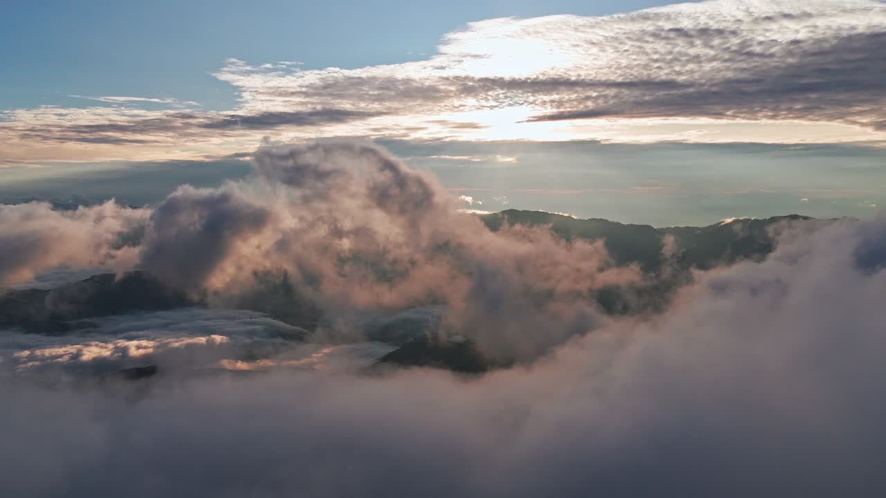 Cinematic aerial view of sun rays (God rays) piercing through dramatic storm clouds over a mountain silhouette. A moody sunrise in the Marilog District highlands creating a spiritual atmosphere