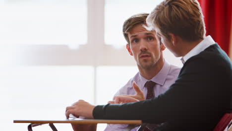 Male-College-Student-Sitting-Examination-Talking-With-Teacher