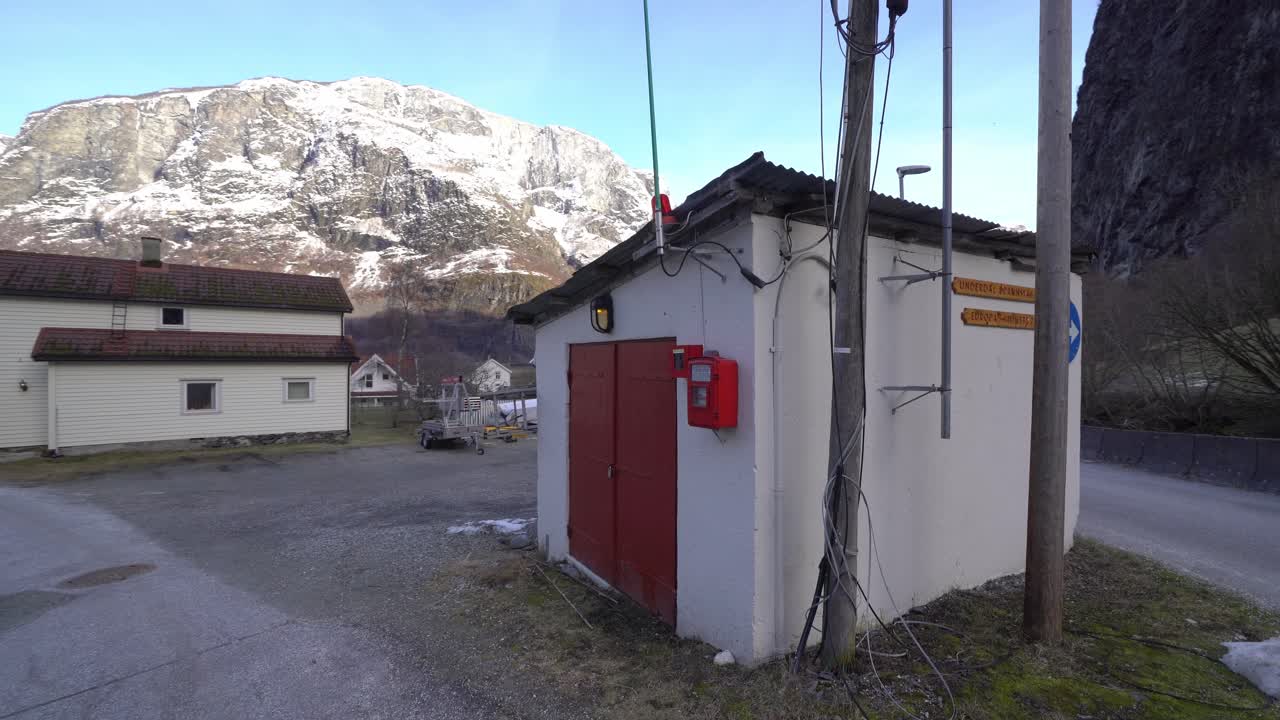estación de bomberos más pequeña de europa ubicada en undredal noruega - girando lentamente alrededor de la estación de bomberos a nivel del suelo con fondo de montaña nevada