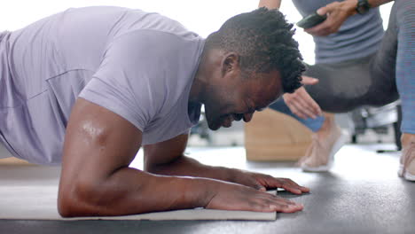 hombre afroamericano en forma haciendo flexiones en el gimnasio con un entrenador