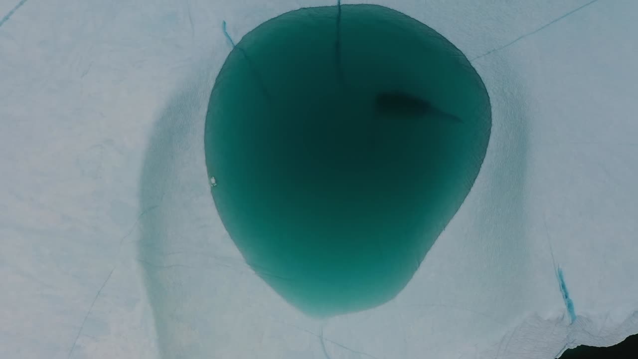Aerial drone view of a deep blue meltwater pool formed on the surface of an iceberg in the Arctic Sea near Greenland, revealing stunning natural texture and vibrant icy contrast