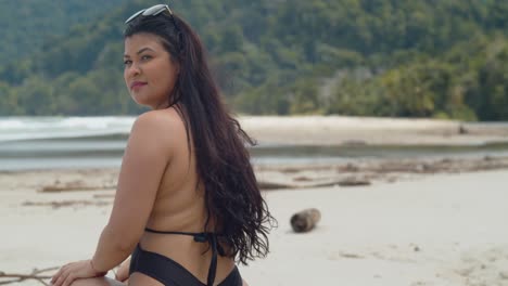 Sexy-female-sitting-on-a-log-at-the-beach-before-turing-around-with-the-waves-of-the-ocean-in-the-background