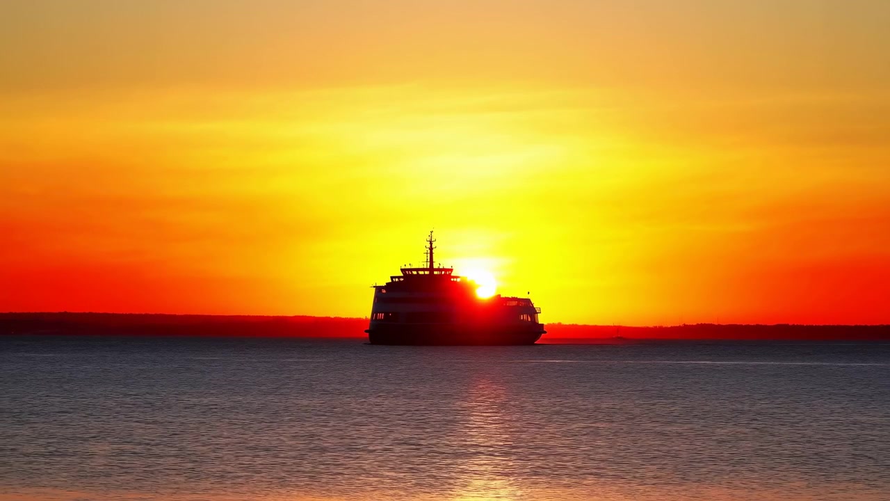 a steady view of a tranquil sunset over the ocean, featuring a ship in silhouette against the vibrant orange and yellow hues of the sky. the calm water reflects these colors, creating a ser.