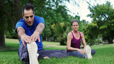 Mature-couple-performing-stretching-exercise-in-the-park
