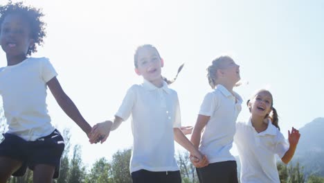 school kids holding hands and jumping in park